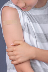 Teenage boy with adhesive bandage plaster on his arm after vaccination on blue background. Injection covid vaccine, healthcare for children and teenagers
