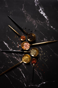 Golden spoons with spices on dark marble