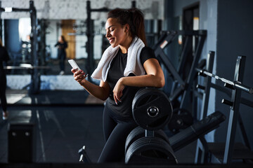 Joyful young woman using smartphone during workout indoors