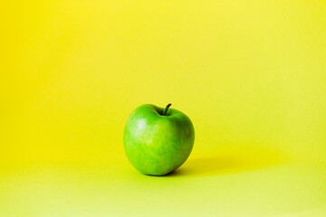 Green apple stands in the middle against a bright yellow background.
