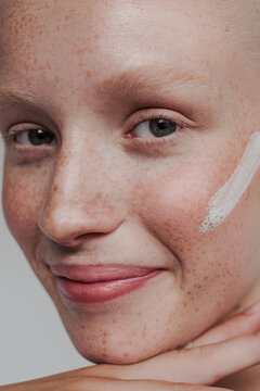 Freckled model with white clay mask on her face smiling