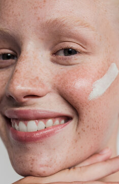 Freckled model with white clay mask on her face smiling