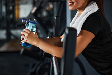 Cheerful young woman quenching thirst in gym