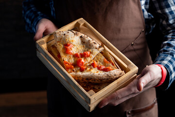 Waiter is holding a cold pizza leftovers, put in a wooden basket, close up, hands only visible