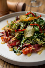 Gourmet restaurant salad with mixed greens, roast beef and potato  chips, wooden table in a restaurant