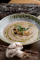 Button mushrooms cream soup with olive oil, old wood and mushrooms around, menu setting