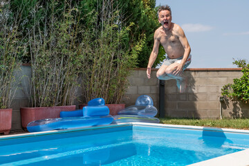 White man with a funny expression takes a cannon ball dive in a swimming pool on a sunny day