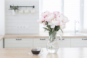 Bouquet of pink peonies and a cup of coffee. Modern interior in the kitchen. Wedding and festive style.