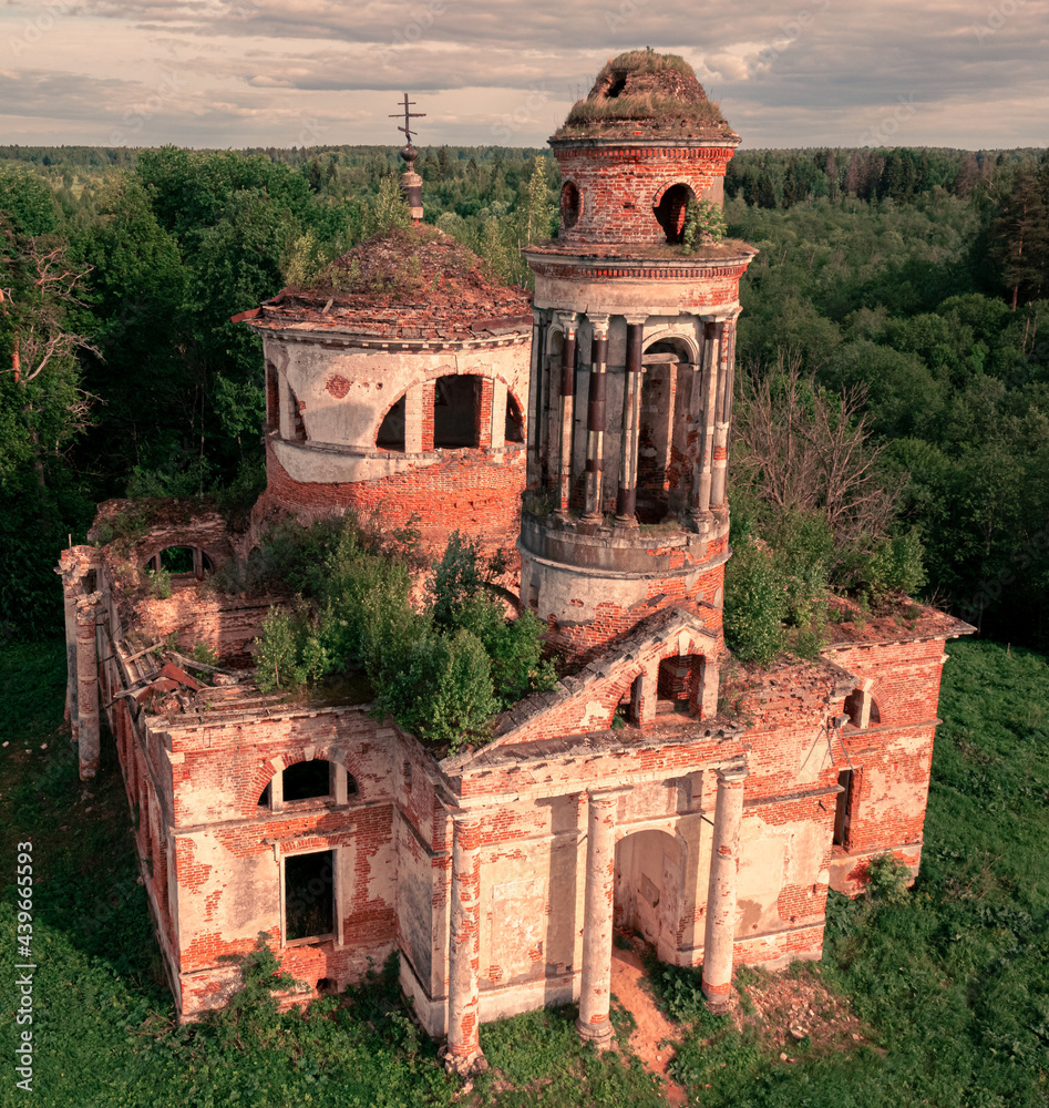 Sticker abandoned church with growing plants on the roof in the forest under a cloudy sky