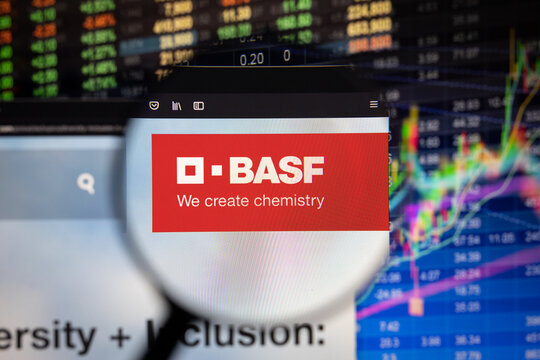 BASF company logo on a website with blurry stock market developments in the background, seen on a computer screen through a magnifying glass	