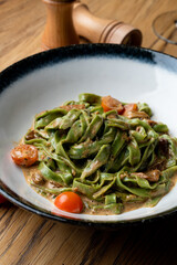 Waitress is sprinkling grated parmesan on spinach fettuccine side view on a wooden table