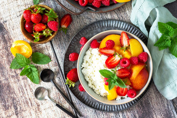 Rustic summer breakfast or dessert. Curd or cottage cheese served with fresh summer fruits and berries on a wooden table. Top view flat lay. Copy space.