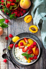 Fototapeta na wymiar Rustic summer breakfast or dessert. Curd or cottage cheese served with fresh summer fruits and berries on a wooden table. Top view flat lay.
