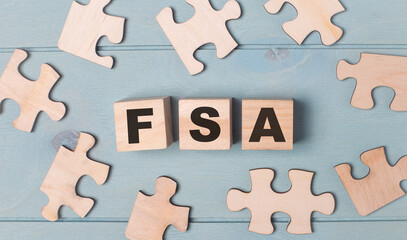 Obraz premium Blank puzzles and wooden cubes with the FSA Flexible Spending Account lie on a light blue background.