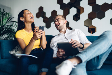 Young man and woman laughing while using gadgets