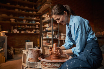 Laughing Caucasian craft woman modeling earthenware in pottery workshop