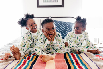 Three siblings in matching pajamas sitting on the bed. 