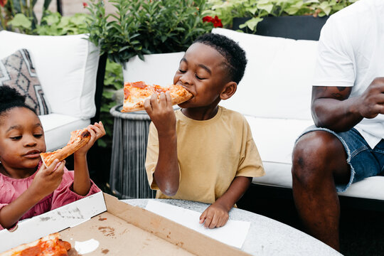 An African American family gathered around a table eating pizza. 