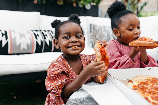 Two little girls having fun eating pizza outdoors with their family. 
