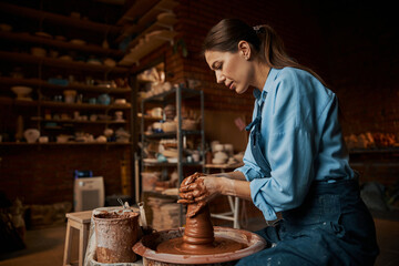 Focused brunette female artisan modeling ceramic tableware in pottery workshop