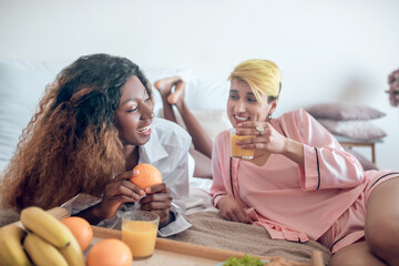 Two young girlfriends laughing having breakfast in bedroom