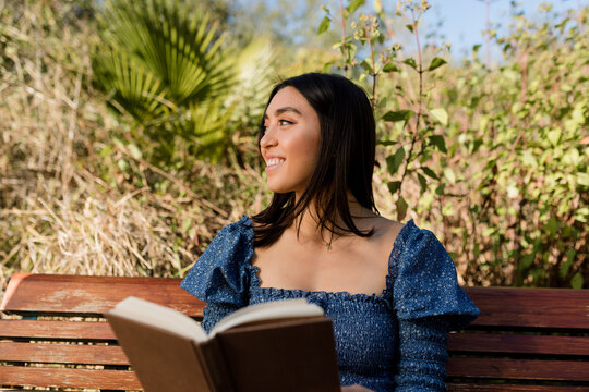 Woman Smiles While Holding a Book in the Park