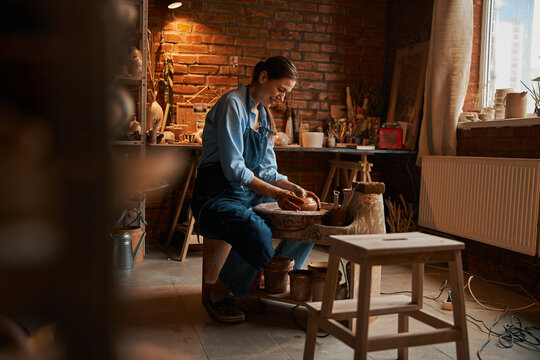 Beautiful young Caucasian female artisan working with fresh wet clay in pottery workshop - Powered by Adobe
