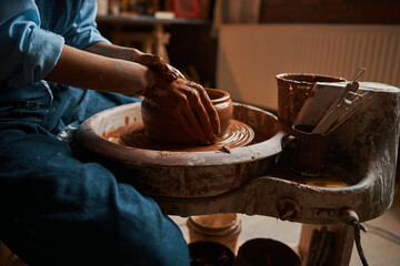 Elegant hands of ceramicist modeling something from fresh wet clay in pottery workshop