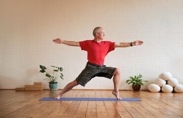 Senior man doing sport on a yoga mat in the studio. Fit healthy elder man practicing ypga. Elderly man keeping fit by exercising her body and mind. - 439670356