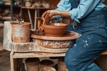 Unrecognized ceramicist modeling clay bowl in pottery workshop