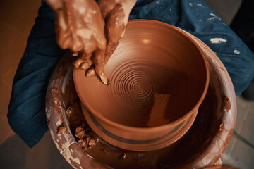 beautiful female hands using special tool while making tableware in pottery workshop