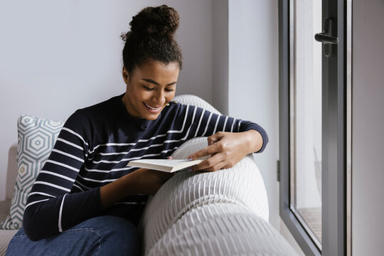 Tender Hispanic woman reading book besides a window