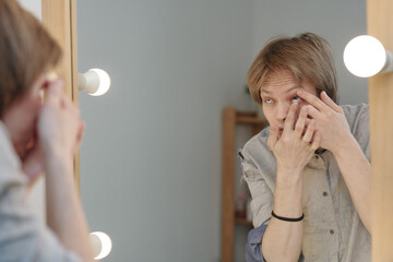 Young man putting contact lens in front of mirror in studio