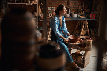 Beautiful elegant female artisan resting during the delicate process manufacturing of ceramic tableware in pottery workshop