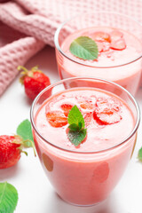 Fresh strawberry milkshake decorated with berries and mint on a light background in pastel colors, space for text, the concept of a healthy breakfast, diet and good nutrition.