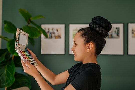 Pre-teen girl looking at an eyeshadow palette mirror by dining room at home