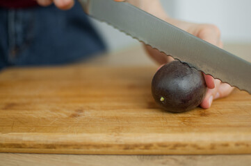 Female hands is cutting a fresh ripe passion fruit, maracuya on a cut wooden board. Exotic fruits, healthy eating concept