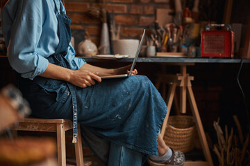 Beautiful elegant young sculptor spending time in pottery workshop while using internet in pottery workshop