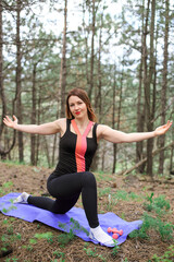 A young woman does yoga on a mat in a pine forest