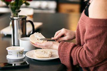 Home: Woman Spreads Cream Cheese On Bagel For Breakfast