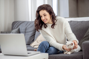Dark-haired woman working on a laptop and hugging her cat
