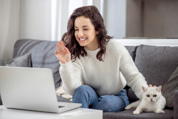 Dark-haired woman working on a laptop and hugging her cat