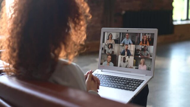 Red-haired curly woman sitting at the laptop, chatting with friends or colleagues via video meeting, discussing the new project, teaching online,making video call to group of diverse people
