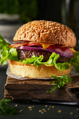 Tasty grilled homemade burgers with beef, tomato, cheese, bacon and lettuce on rustic wooden background. fast food and junk food concept.