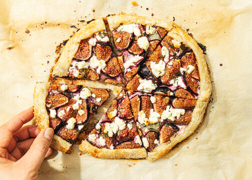 Hand holding slice of fig, thyme and goat cheese galette