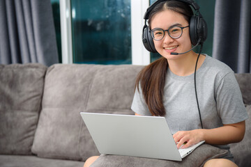Asian young woman student with headphones sitting on the sofa smile looking up happy study online class college learning internet education, Teenage girl work distance on a laptop computer from home