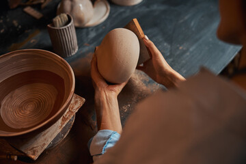 Beautiful young craft woman shaping clay pot in pottery workshop