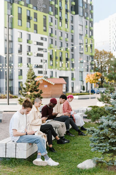 Multiracial men and women using gadgets on bench