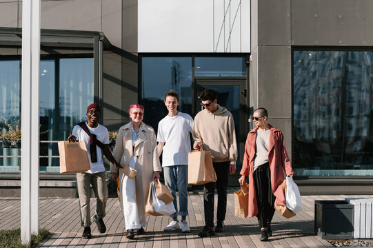 Delighted multiethnic friends with paper bags walking on street