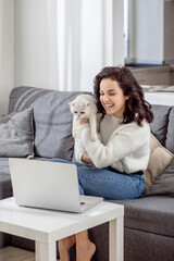 Dark-haired young woman hugginh her cat and having a video call